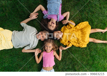 Happy friends lying in the grass, holding each other hands and having fun. Top view. 99663215