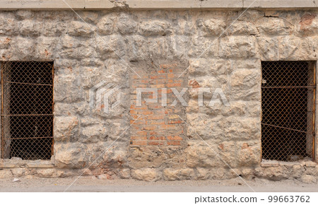 lattice windows on an old stone wall of untreated natural stones and one bricked window. textured background. 99663762