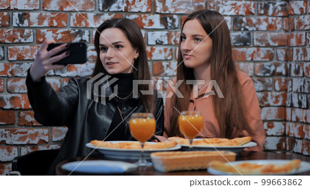 Two girls are sitting in a cafe and taking a selfie on the phone. 99663862