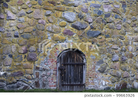 Antique stone wall with wooden door. Part of a historical stone building of past centuries. Antique stone wall with wooden door. Part of a historical stone building of past centuries. 99663926
