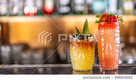 Mai tai cocktails in hawaiian glasses garnished with pineapple, blueberries and strawberries on bar counter. 99664082