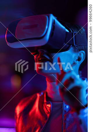 surprised woman in virtual reality goggles on dark surprised woman in virtual reality goggles on dark 99664260