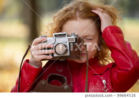Little red-haired girl with a retro camera on an autumn background. Little red-haired girl with a retro camera on an autumn background. 99664516