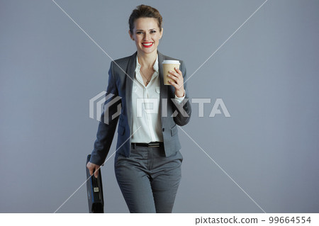 smiling stylish business owner woman walking against grey 99664554