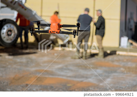On construction site an inspector monitors how concrete is being poured by employees near newly constructed home with help of drone On construction site an inspector monitors how concrete is being poured by employees near newly constructed home with help of drone 99664921