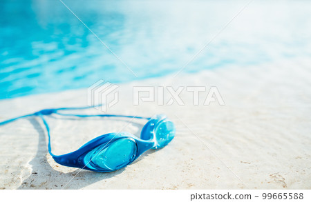 Blue Goggles on the side of swimming pool or seaside. Water and sand. Sunlit. Summer leisure activity and sports concept. Copy space 99665588