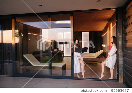Two gorgeous female in luxury resort have rest after sauna. Woman in white bathrobe 99665627