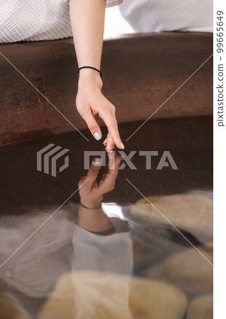 Close-up of female put hand into water of hot tube. Stones inside water 99665649
