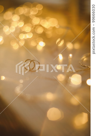 Wedding rings on blured bokeh glowing golden background. Symbol of love and romance on a textured glitter background with copy space for your greeting or congratulations Wedding rings on blured bokeh glowing golden background. Symbol of love and romance on a textured glitter background with copy space for your greeting or congratulations 99666030