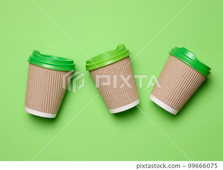 Brown disposable coffee and tea cups made of corrugated cardboard with green plastic lids on green background, top view Brown disposable coffee and tea cups made of corrugated cardboard with green plastic lids on green background, top view 99666075