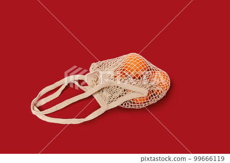 Oranges in a string bag on ruby red background Oranges in a string bag on ruby red background 99666119
