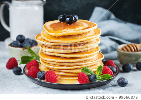 Delicious pancakes, with fresh blueberries, raspberry and maple syrup or honey on a dark background Delicious pancakes, with fresh blueberries, raspberry and maple syrup or honey on a dark background 99666879