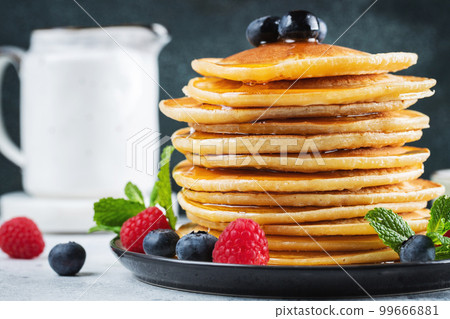 Delicious pancakes, with fresh blueberries, raspberry and maple syrup or honey on a dark background Delicious pancakes, with fresh blueberries, raspberry and maple syrup or honey on a dark background 99666881
