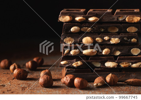 Dark and milk chocolate with nuts on a dark background sprinkled with cocoa powder. Dark and milk chocolate with nuts on a dark background sprinkled with cocoa powder. 99667745