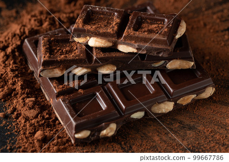 Dark and milk chocolate with nuts on a dark background sprinkled with cocoa powder. 99667786