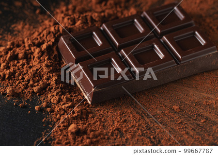 Dark and milk chocolate with nuts on a dark background sprinkled with cocoa powder. 99667787
