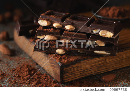 Dark and milk chocolate with nuts on a dark background sprinkled with cocoa powder. 99667788
