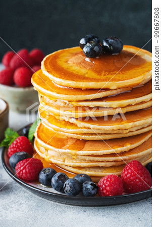 Delicious pancakes, with fresh blueberries, raspberry and maple syrup or honey on a dark background 99667808