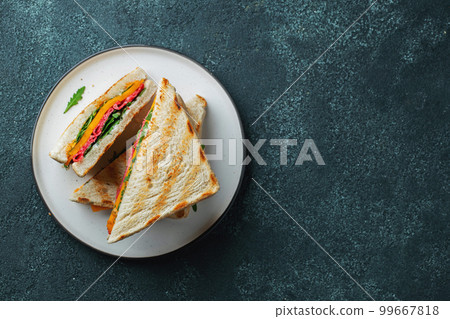 Three homemade sandwiches with sausage, cheese and arugula on a dark concrete background 99667818