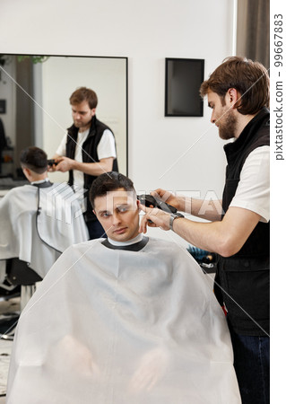 Barber shaving caucasian man in barber shop. Barber shaving caucasian man in barber shop. 99667883
