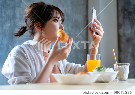 Generation Z young woman using smartphone while eating breakfast 99671536