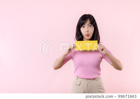 Portrait happy young woman model holding and showing blank space paper for advertisement information message poster with thumb up or point finger gesture isolated on pink pastel studio background. Portrait happy young woman model holding and showing blank space paper for advertisement information message poster with thumb up or point finger gesture isolated on pink pastel studio background. 99671663