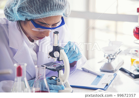 Asian Woman scientist hand write note research in medical lab look at science microscope medical test. Researcher biology chemistry. Asian Female technician laboratory using microscope blood test 99672357