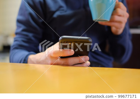 Man drinking coffee while looking at smartphone at home 99677171