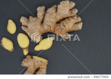 Ginger rhizome with slices on black stone background Ginger rhizome with slices on black stone background 99677909