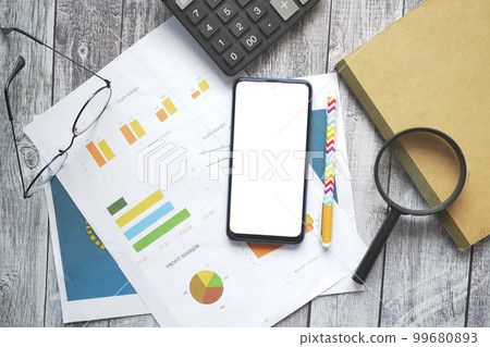 top view of smart phone with empty screen and financial chart on table top view of smart phone with empty screen and financial chart on table 99680893