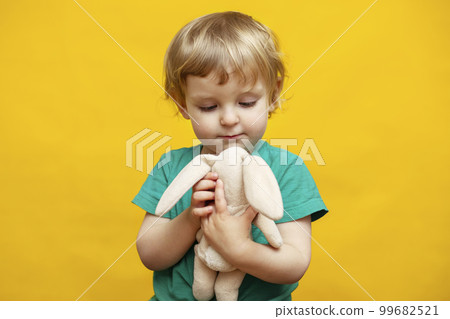 Cute little kid hugging a plush rabbit bunny toy on yellow background 99682521