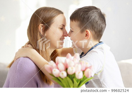 Cute son giving his mother bouquet of tulips congratulating her on mothers day Cute son giving his mother bouquet of tulips congratulating her on mothers day 99682524