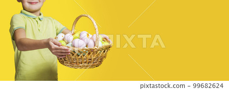 Little child holding basket with painted eggs on yellow background. Easter day 99682624
