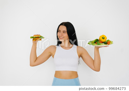 Young woman makes a choice between healthy and unhealthy food on a white background Young woman makes a choice between healthy and unhealthy food on a white background 99684273