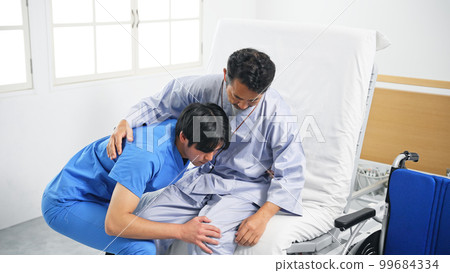 Caregiver assisting transfer from bed to wheelchair 99684334