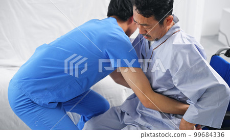 Caregiver assisting transfer from bed to wheelchair 99684336