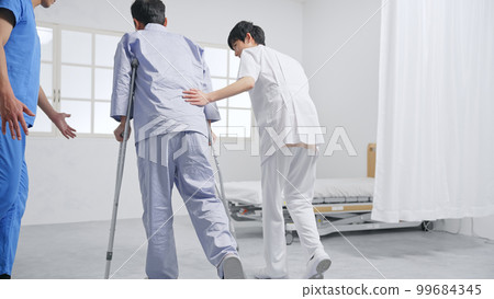 Patient and care staff rehabilitating with crutches 99684345