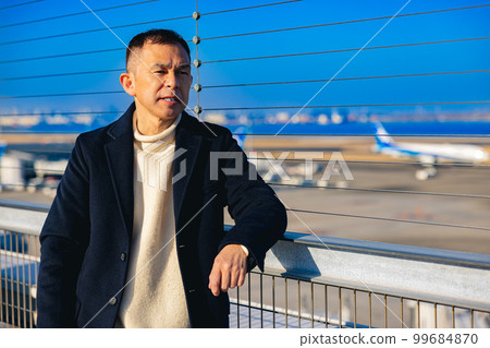 A middle-aged man waiting for an overseas trip departure on the observation deck 99684870