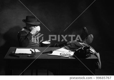 Black and white, noir, vintage photography. Man, professional detective in hat sitting at table and drinking coffee. Investigation 99685767
