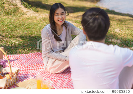Young couple in love talking and picnic together while on blanket near lake in the park 99685830