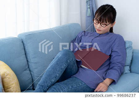 A woman taking a nap while reading a book on the sofa A woman taking a nap while reading a book on the sofa 99686237