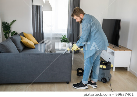 Man holding modern washing vacuum cleaner and cleaning dirty sofa with professionally detergent. Professional springclean at home concept Man holding modern washing vacuum cleaner and cleaning dirty sofa with professionally detergent. Professional springclean at home concept 99687401