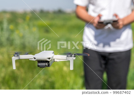 A man a drone pilot with a control panel in his hands controls a quadcopter in the summer field outdoor 99687402