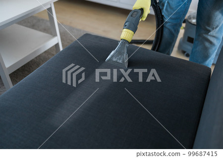 Man dry cleaner's employee hand in protective rubber glove cleaning sofa with professionally extraction method. Early spring regular cleanup. Commercial cleaning company concept Man dry cleaner's employee hand in protective rubber glove cleaning sofa with professionally extraction method. Early spring regular cleanup. Commercial cleaning company concept 99687415