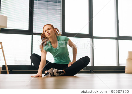 Low-angle view of suffering sporty young woman doing stretching exercises sitting on floor and stop training as feeling leg pain during fitness workout. Female athlete touching leg in injury. Low-angle view of suffering sporty young woman doing stretching exercises sitting on floor and stop training as feeling leg pain during fitness workout. Female athlete touching leg in injury. 99687560