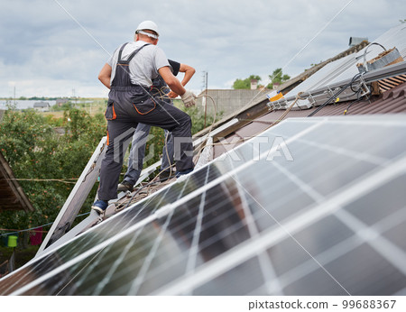 Men technicians lifting up photovoltaic solar moduls on roof of house. Workmen in helmets installing solar panel system outdoors. Concept of alternative and renewable energy. 99688367