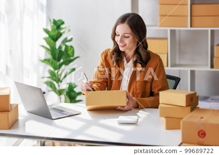 Concept of parcel delivery and selling online,Female seller or retailer write the customer's address on the parcel box to prepare for delivery and using laptop checking day's sales on the online store Concept of parcel delivery and selling online,Female seller or retailer write the customer's address on the parcel box to prepare for delivery and using laptop checking day's sales on the online store 99689722