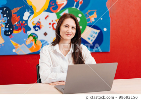 a brunette woman in white shirt works at computer in an office with red walls. a brunette woman in white shirt works at computer in an office with red walls. 99692150