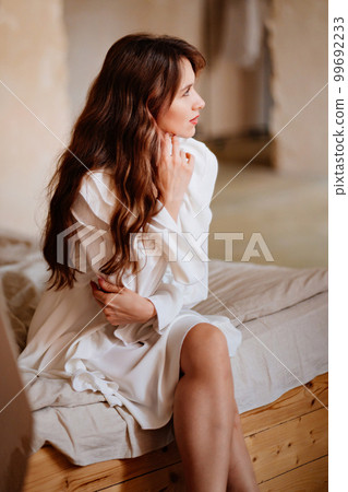 a beautiful woman in a white sexy dress with lacing and ruffles sits on the bed a beautiful woman in a white sexy dress with lacing and ruffles sits on the bed 99692233