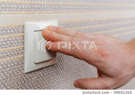 men's hand on White light switch on the wall with brown wallpaper. men's hand on White light switch on the wall with brown wallpaper. 99692268